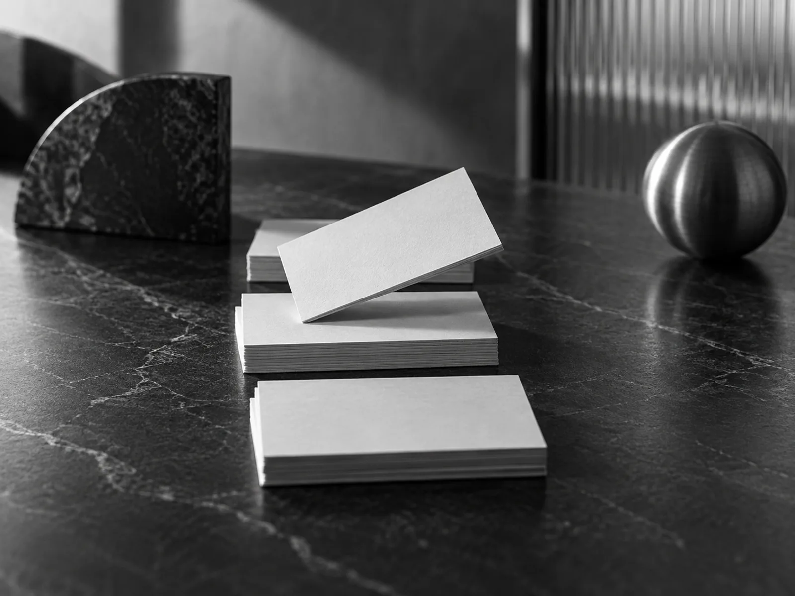 Cartões de papel em branco organizados sobre mesa de pedra escura, com um cartão apoiado em diagonal entre as pilhas