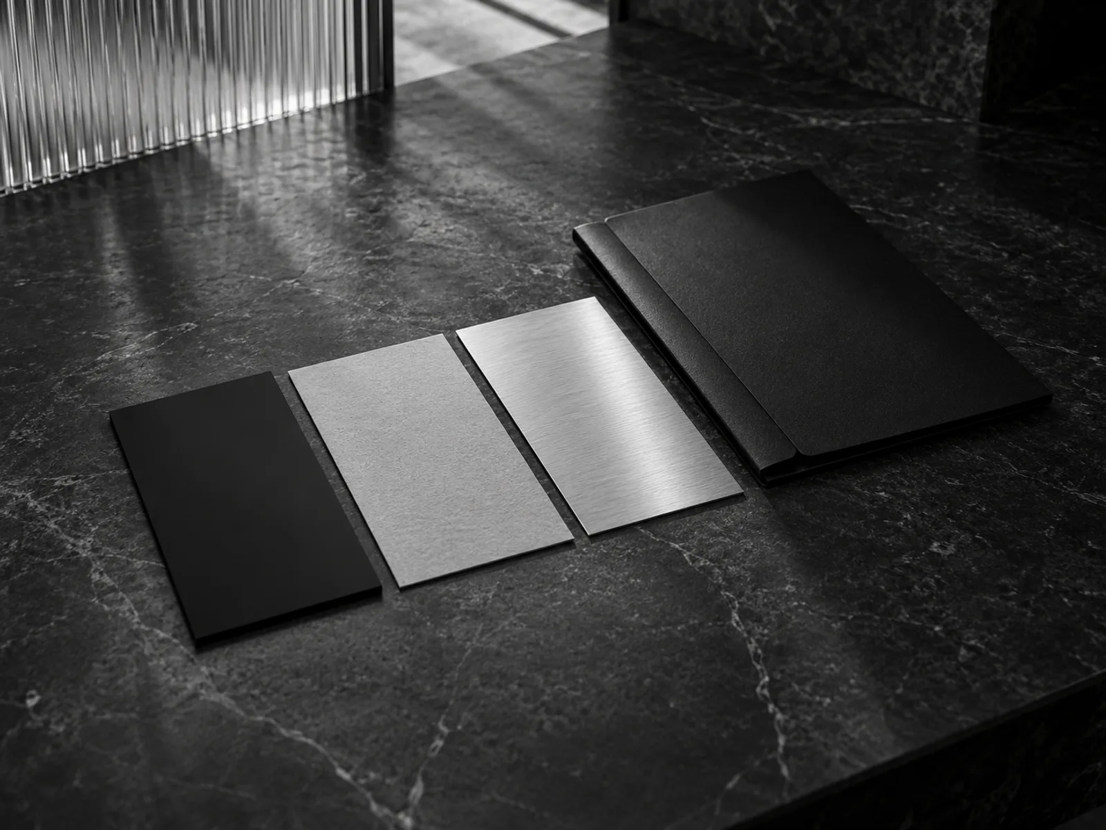 Natureza-morta editorial conceitual em preto e branco com amostras retangulares de materiais alinhadas e uma pasta escura sobre mesa de pedra